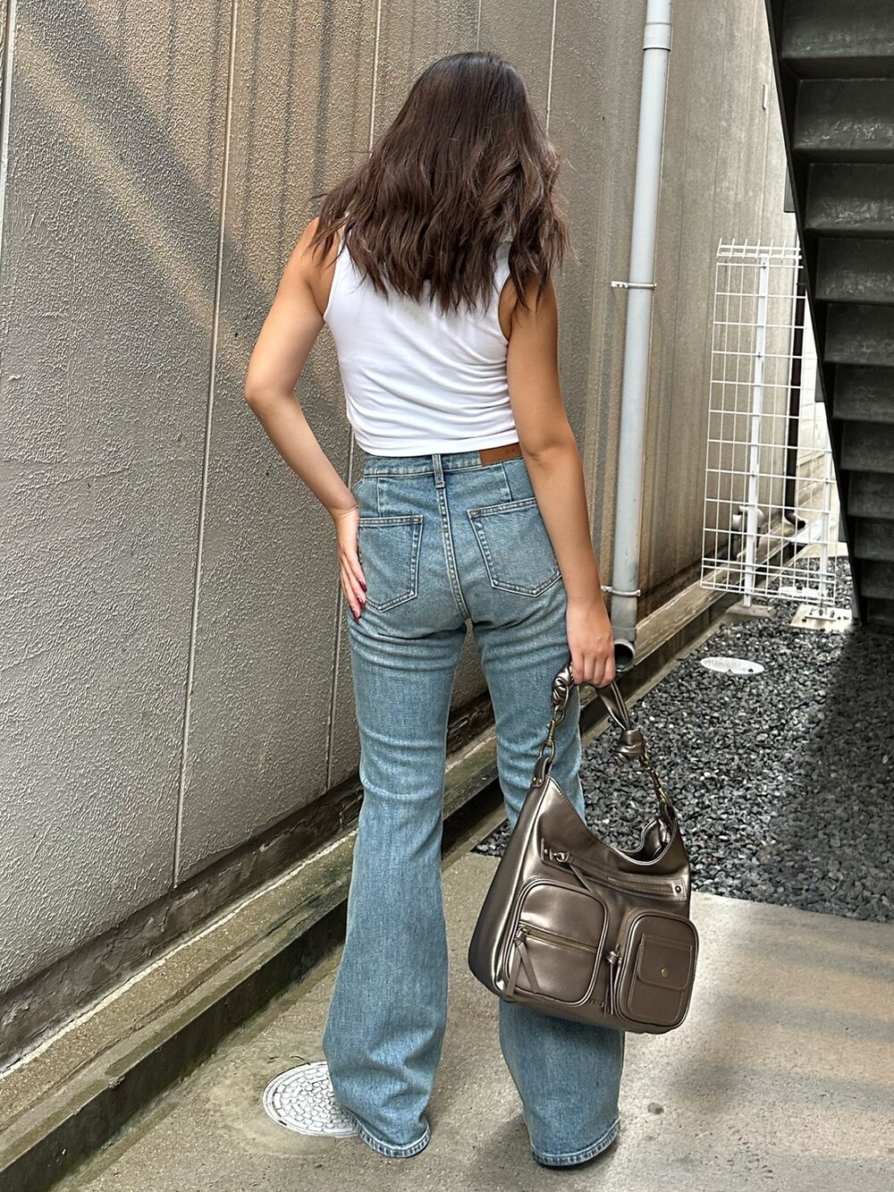 ブルー系のデニムパンツ、ゴールド系のハンドバッグ、ホワイト系のタンクトップを着用したレディースの夏コーディネートの3枚目の写真