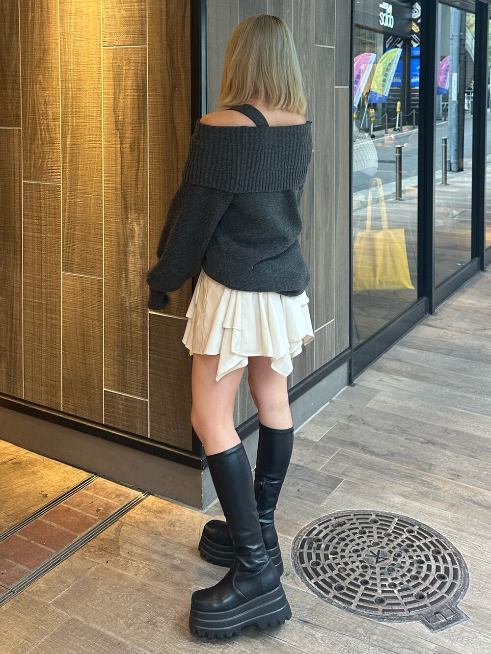 グレー系のワンピース、ホワイト系のスカート、ブラック系のブーツを着用したレディースの秋コーディネートの3枚目の写真