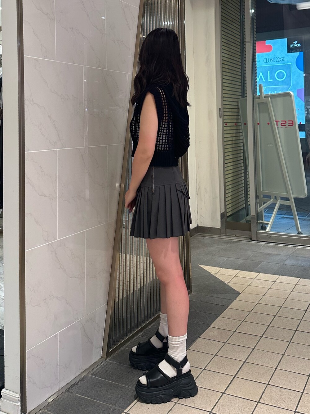 ブラック系のニット/セーター、グレー系のスカート、ブラック系のサンダルを着用したレディースの夏コーディネートの2枚目の写真