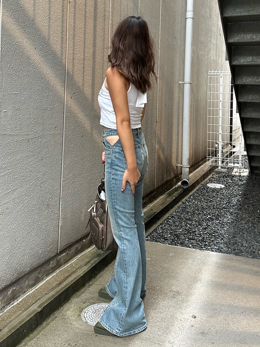 ブルー系のデニムパンツ、ゴールド系のハンドバッグ、ホワイト系のタンクトップを着用したレディースの夏コーディネートの2枚目の写真