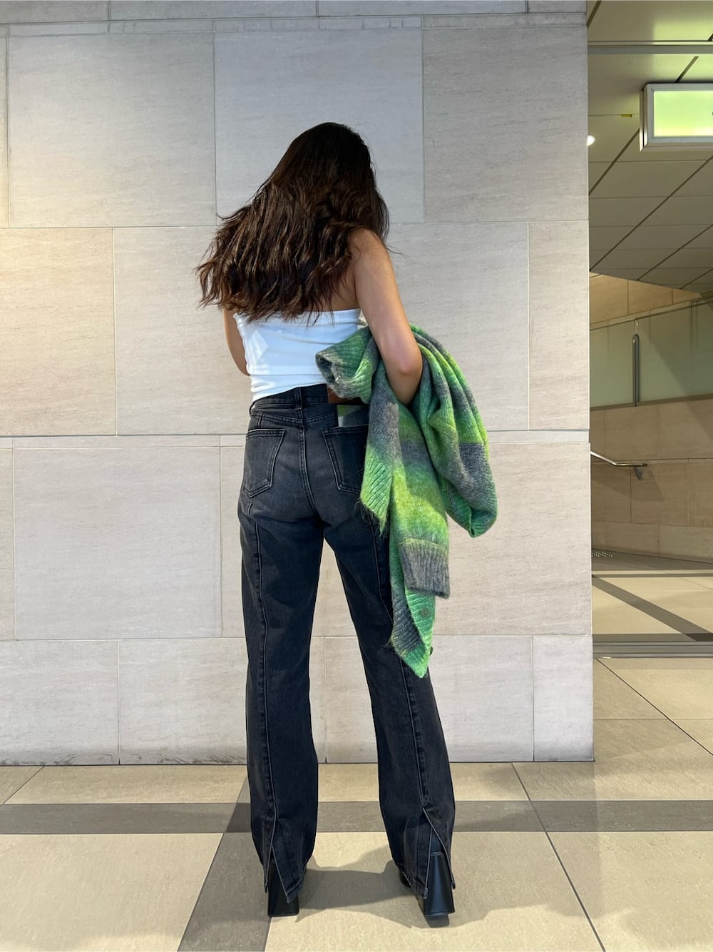 グリーン系のカーディガン/ボレロ、ホワイト系のチューブトップ、ブラック系のデニムパンツを着用したレディースの秋コーディネートの5枚目の写真