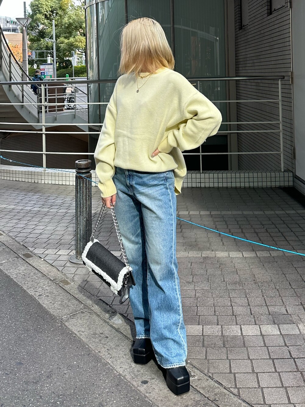 イエロー系のニット/セーター、ブルー系のデニムパンツ、ブラック系のショルダーバッグを着用したレディースの冬コーディネートの2枚目の写真