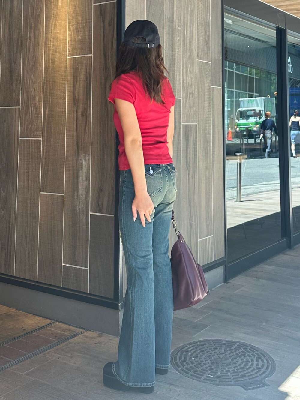 ブルー系のデニムパンツ、レッド系のハンドバッグ、ブラック系のブーツを着用したレディースの秋コーディネートの2枚目の写真