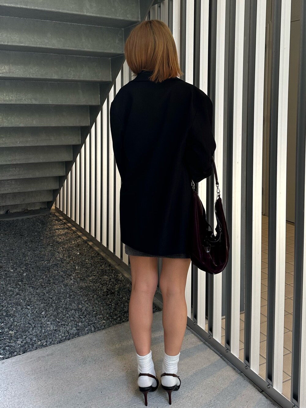 グレー系のワンピース、ブラック系のテーラードジャケット、レッド系のパンプスを着用したレディースの秋コーディネートの4枚目の写真