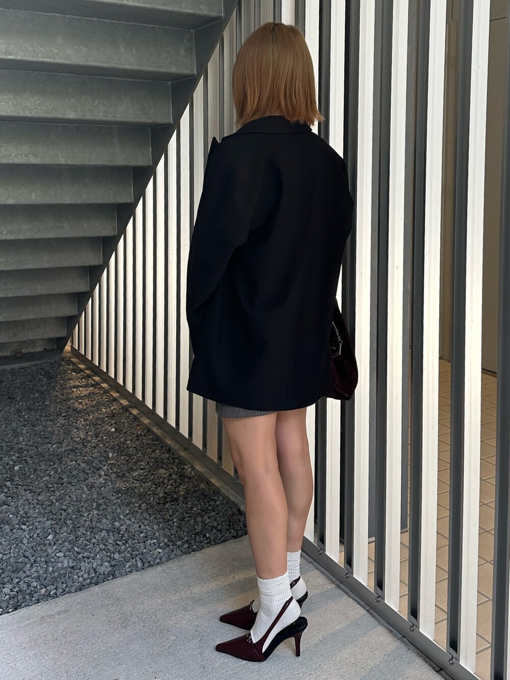 グレー系のワンピース、ブラック系のテーラードジャケット、レッド系のパンプスを着用したレディースの秋コーディネートの3枚目の写真