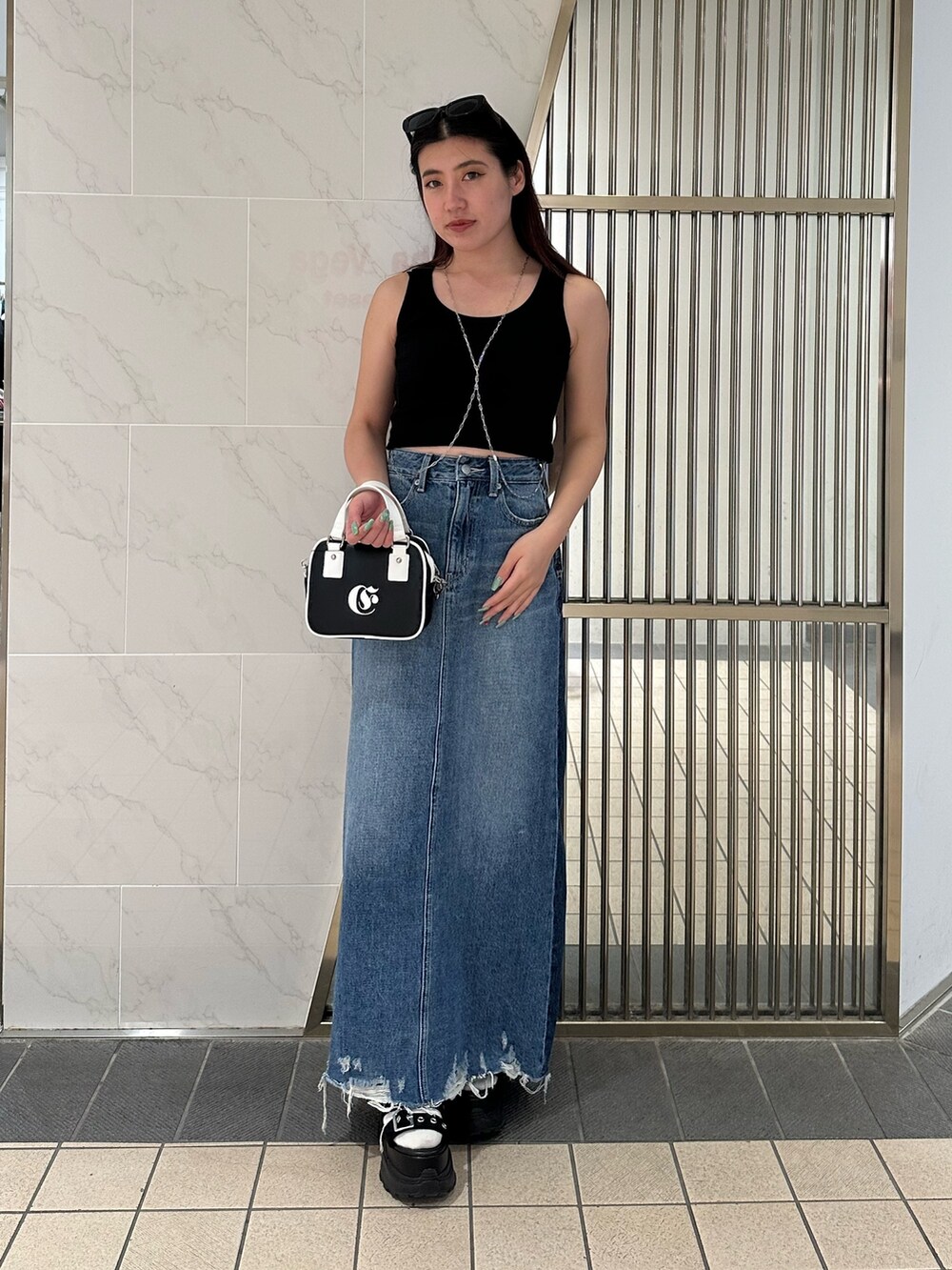 ブルー系のデニムスカート、ブラック系のタンクトップ、ブラック系のサンダルを着用したレディースの春コーディネートの3枚目の写真
