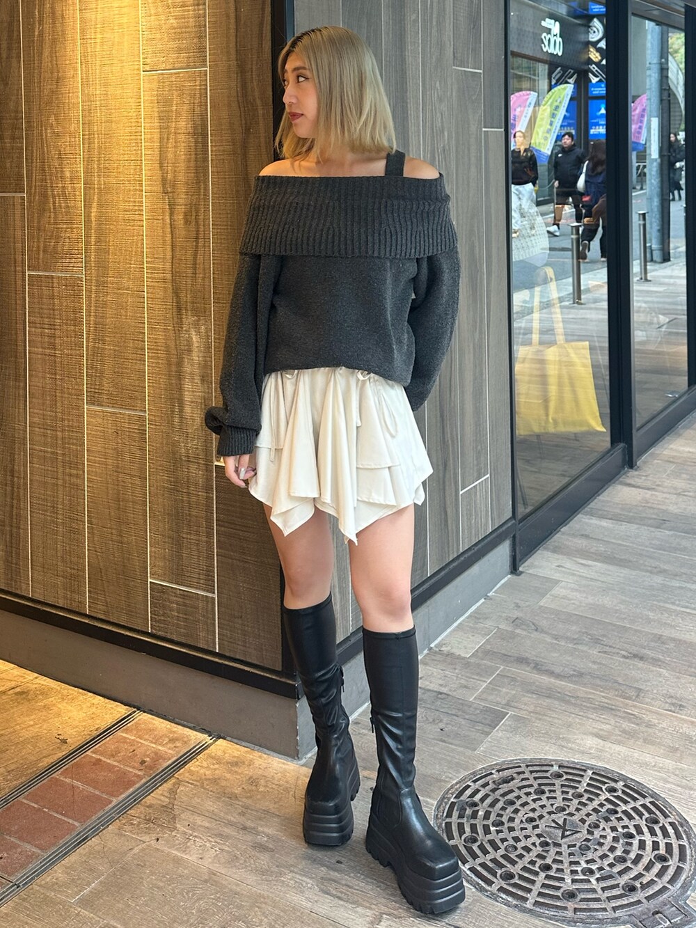 グレー系のワンピース、ホワイト系のスカート、ブラック系のブーツを着用したレディースの秋コーディネートの2枚目の写真