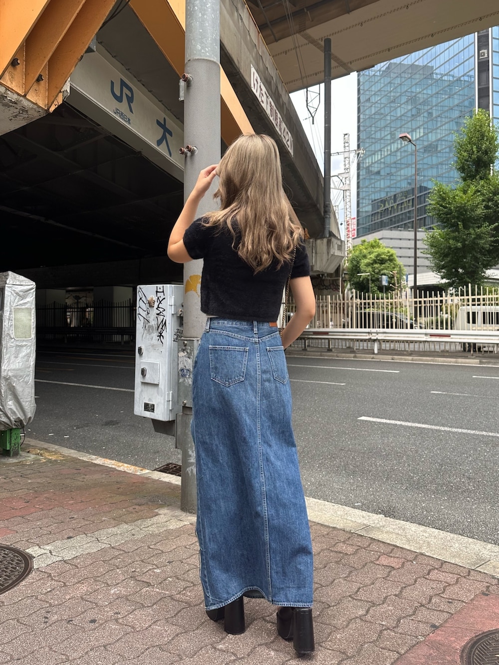 ブルー系のデニムスカート、ブラック系のサンダル、ブラック系のニット/セーターを着用したレディースの夏コーディネートの2枚目の写真