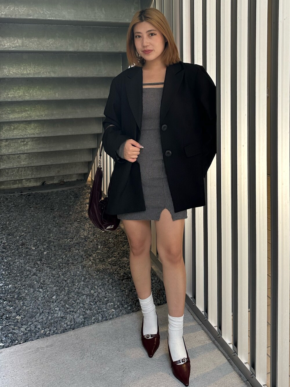 グレー系のワンピース、ブラック系のテーラードジャケット、レッド系のパンプスを着用したレディースの秋コーディネートの2枚目の写真