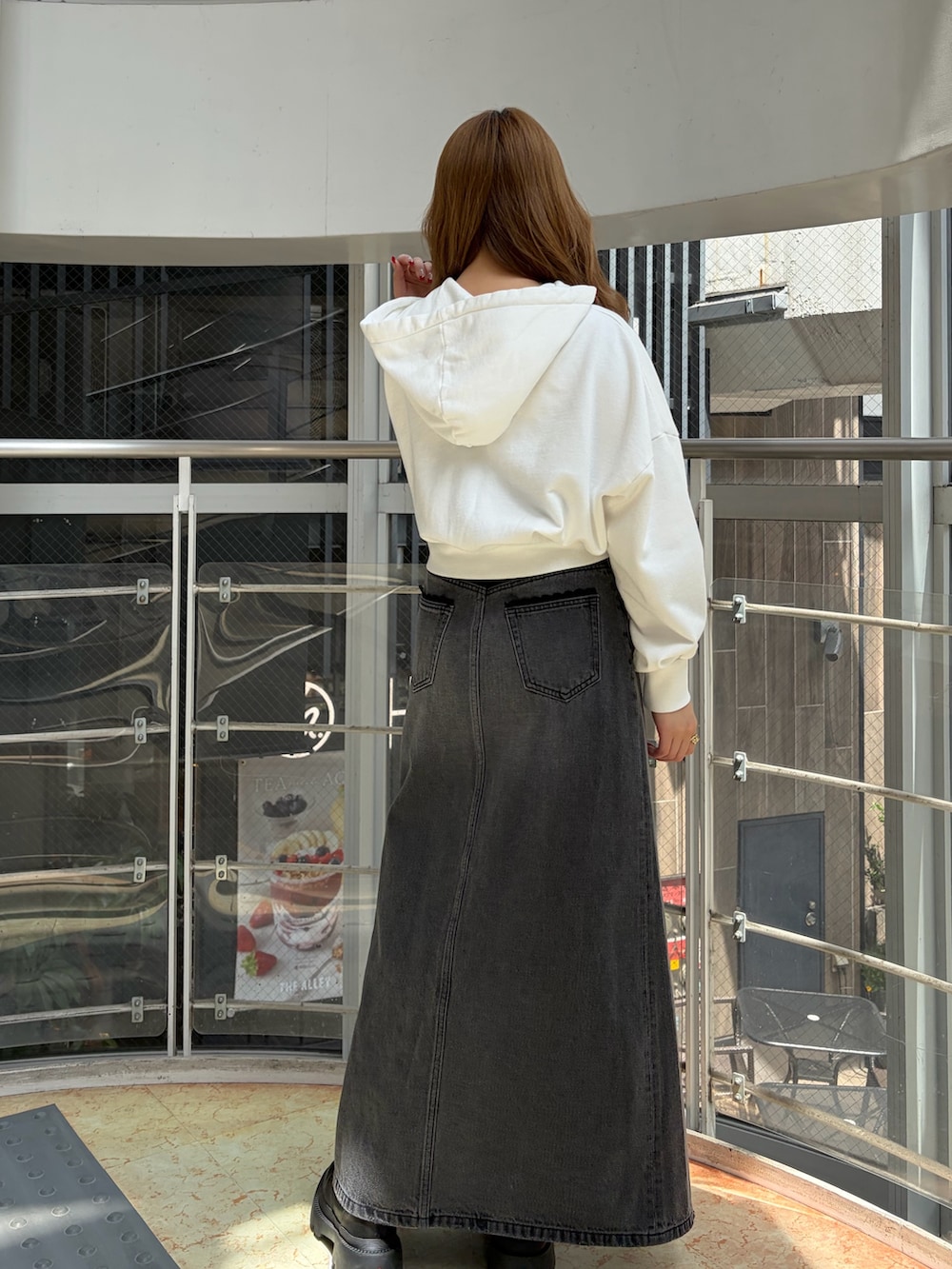 ホワイト系のパーカー、ブラック系のデニムスカート、ブラック系のブーツを着用したレディースの春コーディネートの3枚目の写真