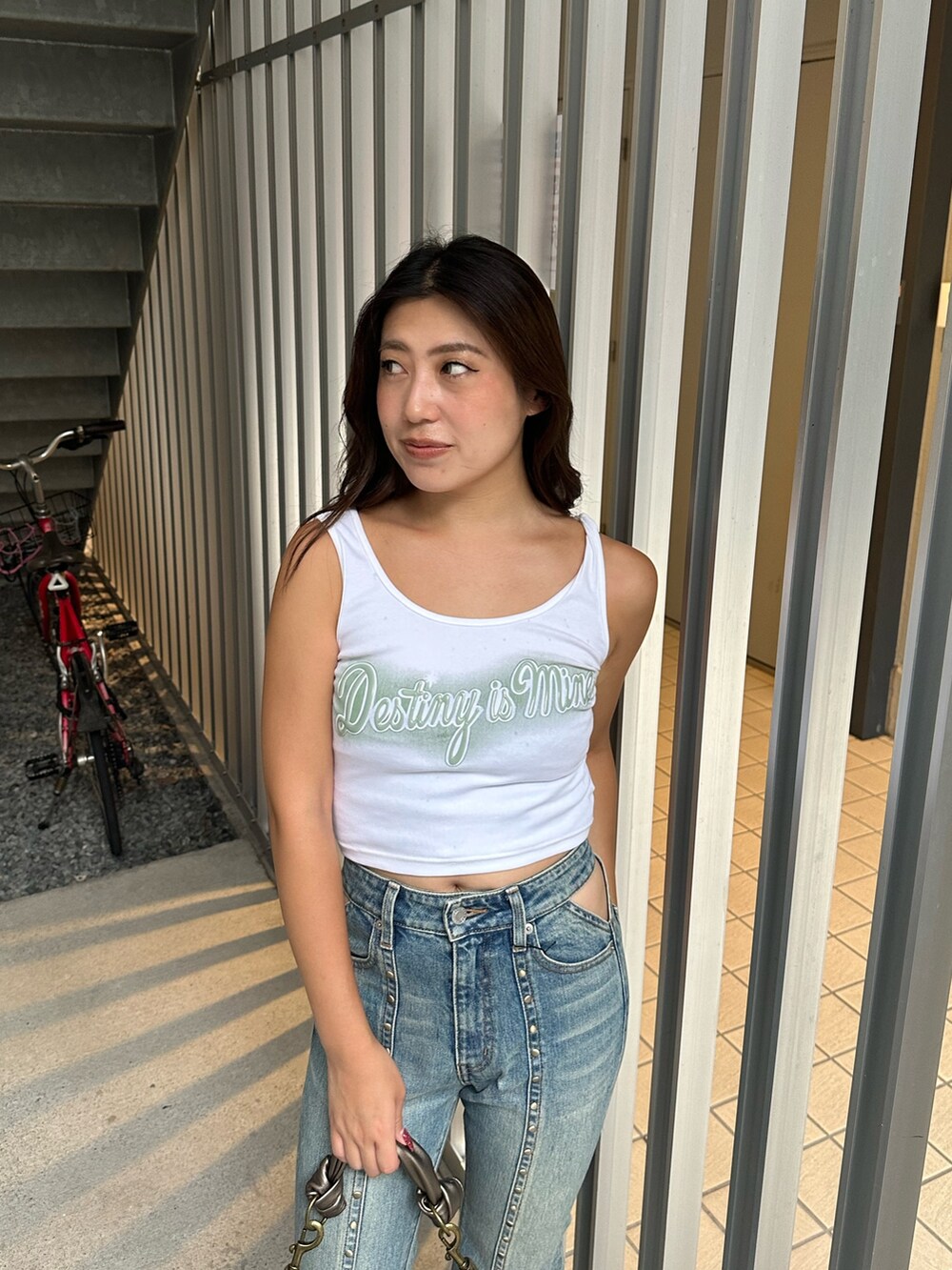 ブルー系のデニムパンツ、ゴールド系のハンドバッグ、ホワイト系のタンクトップを着用したレディースの夏コーディネートの4枚目の写真