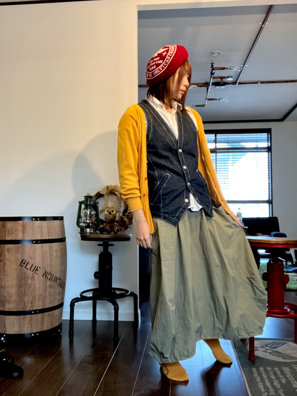 イエロー系のカーディガン/ボレロ、グリーン系のスカート、ブルー系のベストを着用したレディースの秋コーディネートの4枚目の写真