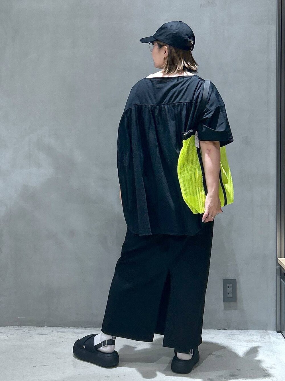 イエロー系のトートバッグ、ブラック系のスカート、ブラック系のサンダルを着用したレディースの夏コーディネートの2枚目の写真