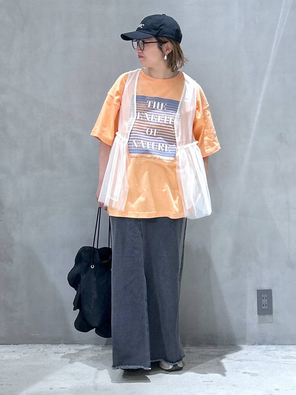 ブラック系のショルダーバッグ、ブラック系のデニムスカート、ベージュ系のベストを着用したレディースの春コーディネートの5枚目の写真