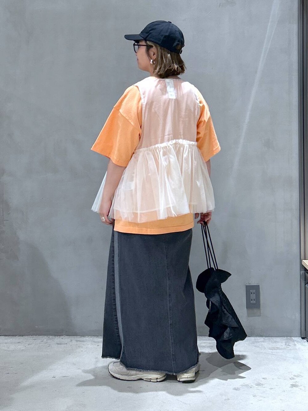 ブラック系のショルダーバッグ、ブラック系のデニムスカート、ベージュ系のベストを着用したレディースの春コーディネートの2枚目の写真