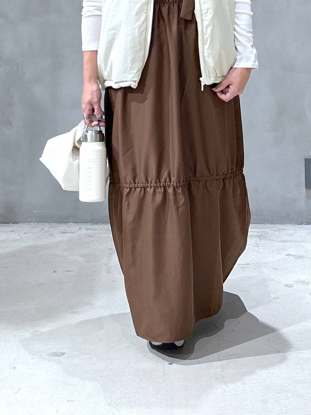 ホワイト系のスニーカー、ベージュ系のベスト、ブラウン系のワンピースを着用したレディースの秋コーディネートの3枚目の写真