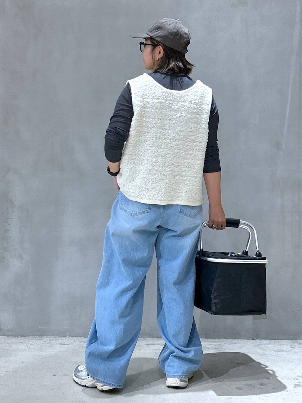 グレー系のスニーカー、ブルー系のデニムパンツ、ベージュ系のベストを着用したレディースの秋コーディネートの2枚目の写真