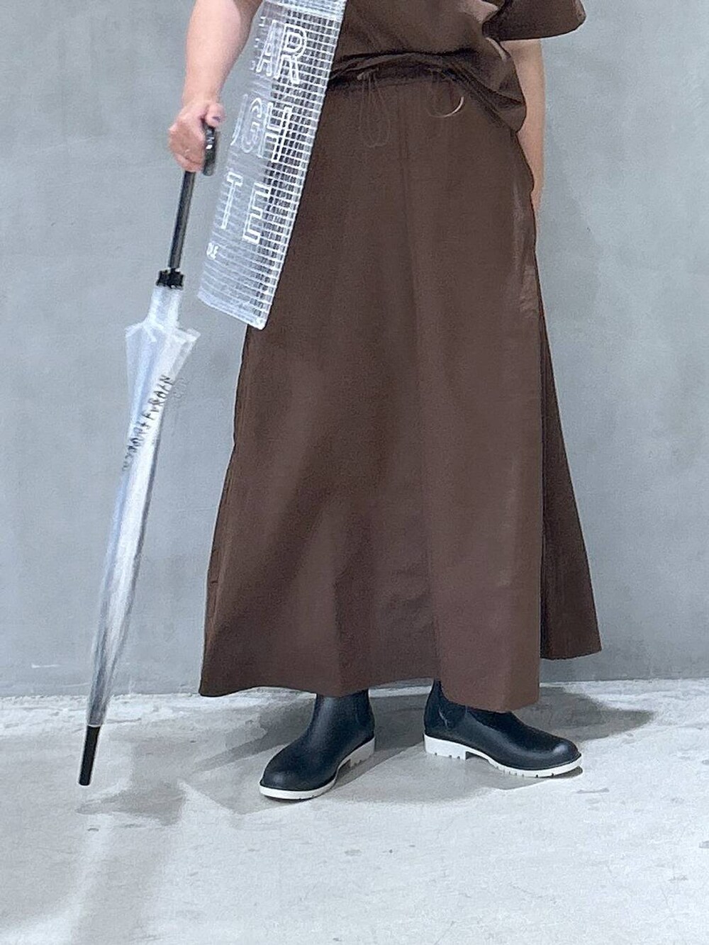 ブラック系のレインシューズ、ブラウン系のTシャツ/カットソー、ブラウン系のスカートを着用したレディースの夏コーディネートの4枚目の写真