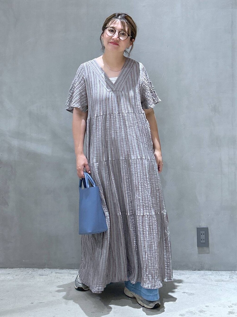 グレー系のワンピース、ブルー系のデニムパンツ、ブルー系のショルダーバッグを着用したレディースの夏コーディネートの5枚目の写真