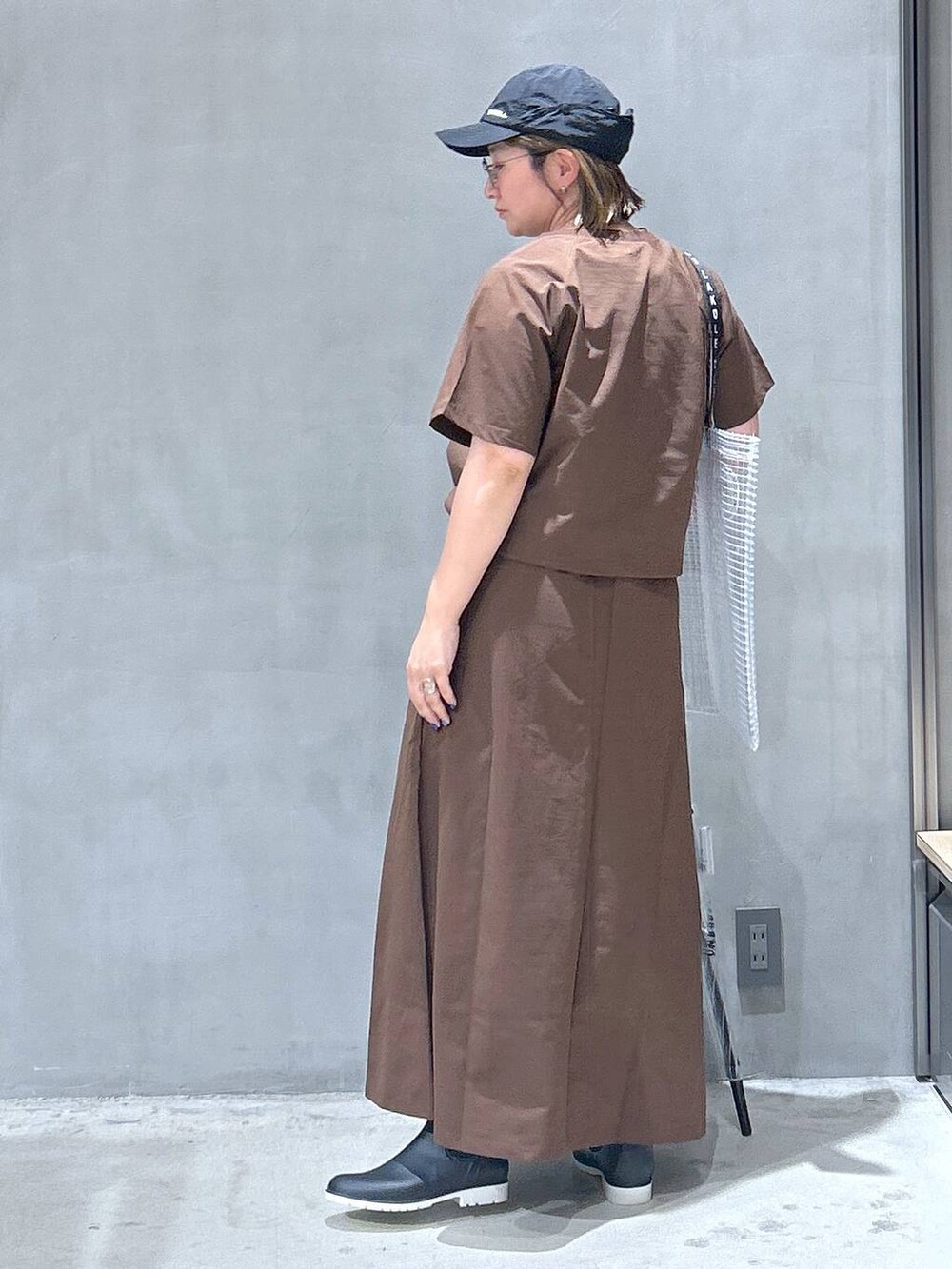 ブラック系のレインシューズ、ブラウン系のTシャツ/カットソー、ブラウン系のスカートを着用したレディースの夏コーディネートの2枚目の写真
