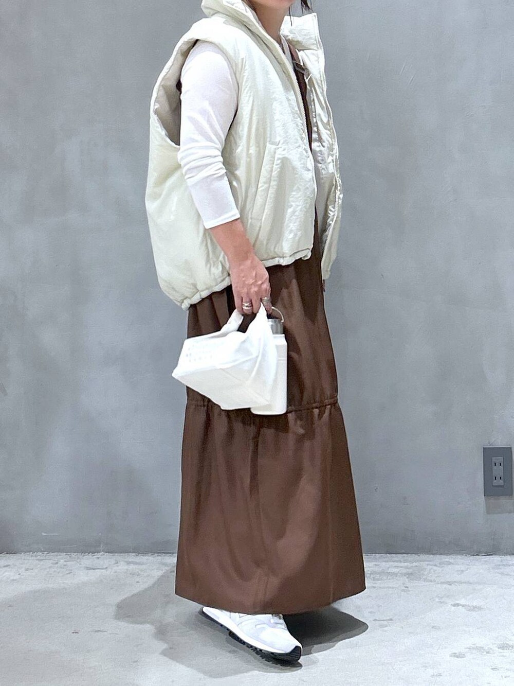 ホワイト系のスニーカー、ベージュ系のベスト、ブラウン系のワンピースを着用したレディースの秋コーディネートの4枚目の写真