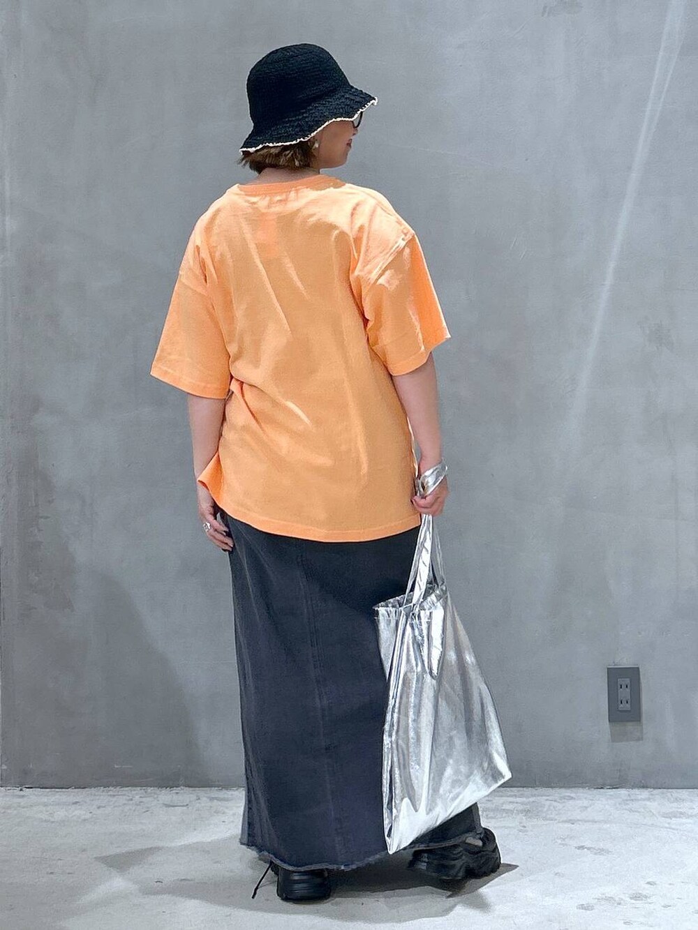 ブラック系のスニーカー、ブラック系のデニムスカート、オレンジ系のTシャツ/カットソーを着用したレディースの春コーディネートの2枚目の写真