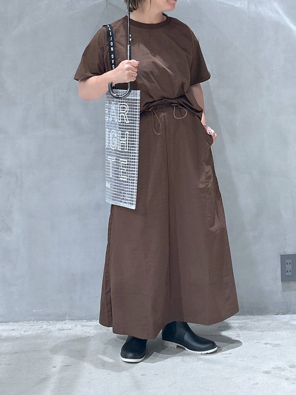 ブラック系のレインシューズ、ブラウン系のTシャツ/カットソー、ブラウン系のスカートを着用したレディースの夏コーディネートの5枚目の写真