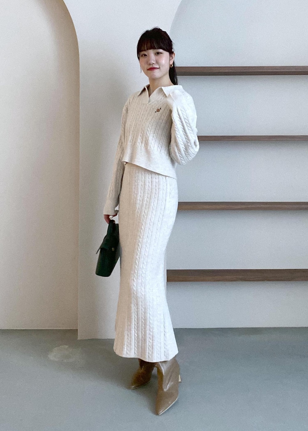 グリーン系のショルダーバッグ、ベージュ系のブーツ、ベージュ系のスカートを着用したレディースの冬コーディネートの2枚目の写真