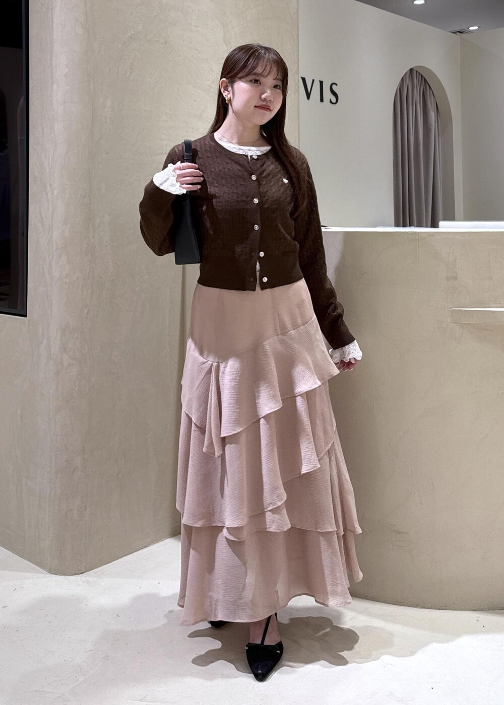 ブラック系のパンプス、ピンク系のスカート、ブラウン系のカーディガン/ボレロを着用したレディースの秋コーディネートの2枚目の写真