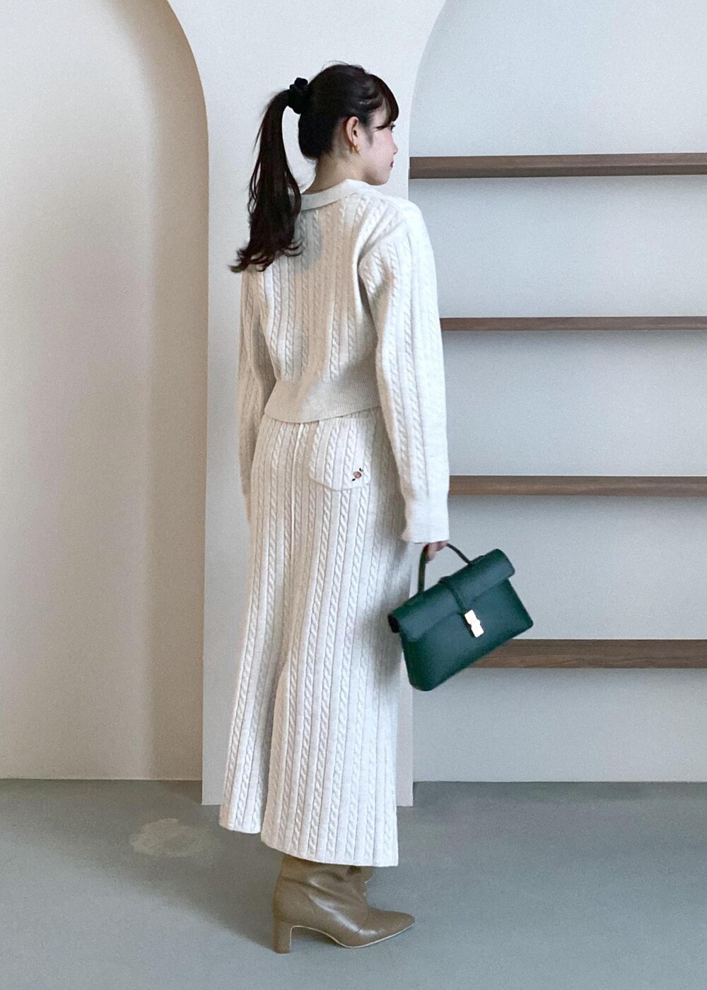 グリーン系のショルダーバッグ、ベージュ系のブーツ、ベージュ系のスカートを着用したレディースの冬コーディネートの5枚目の写真