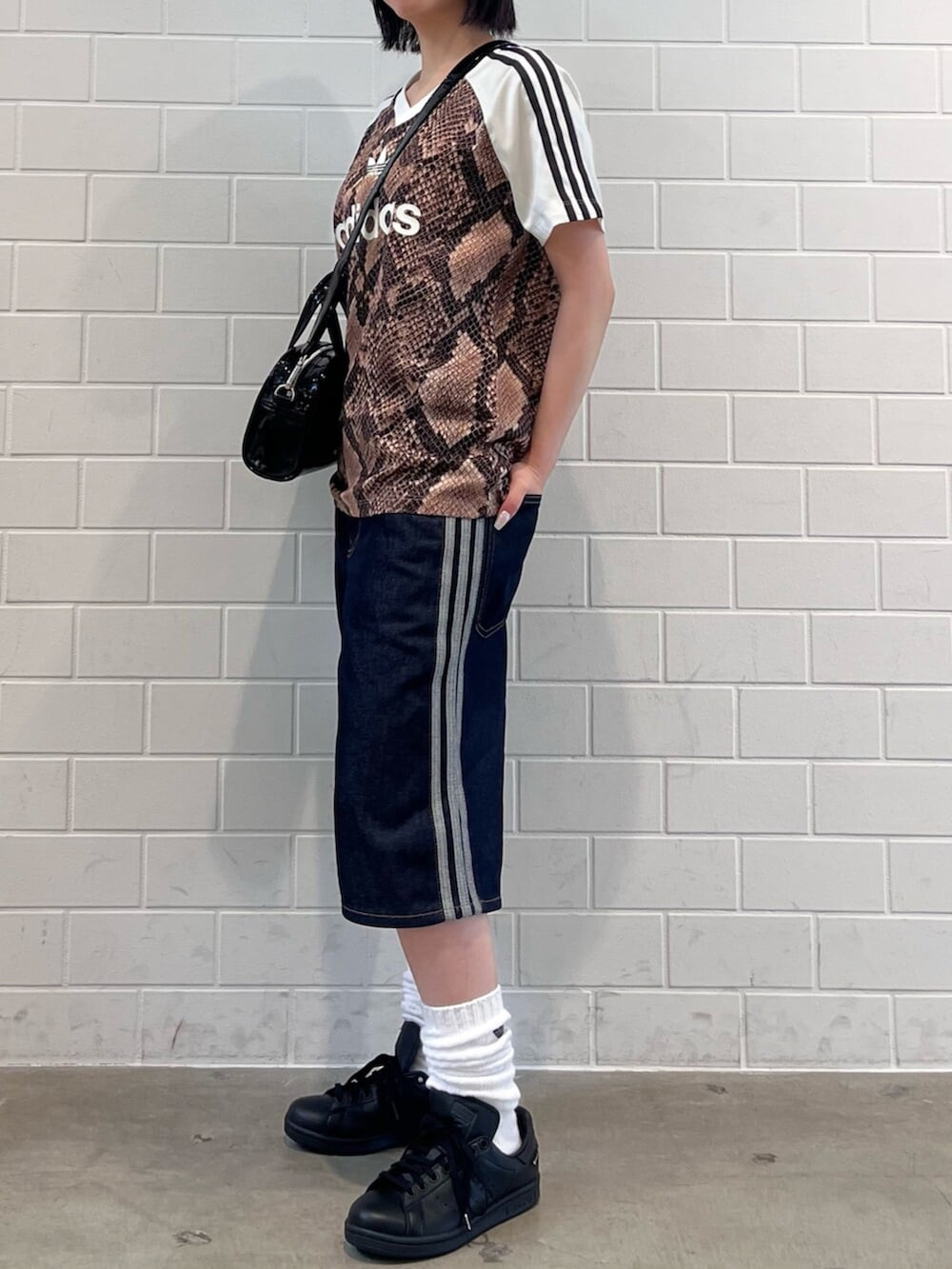 ブラック系のショルダーバッグ、ブルー系のデニムパンツ、ブラック系のスニーカーを着用したレディースの夏コーディネートの2枚目の写真