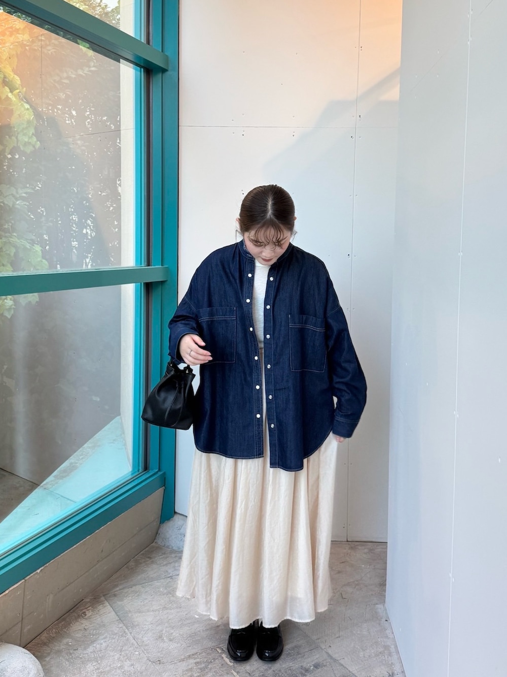 ブラック系のショルダーバッグ、ベージュ系のスカート、ブラック系のレインシューズを着用したレディースの秋コーディネートの2枚目の写真