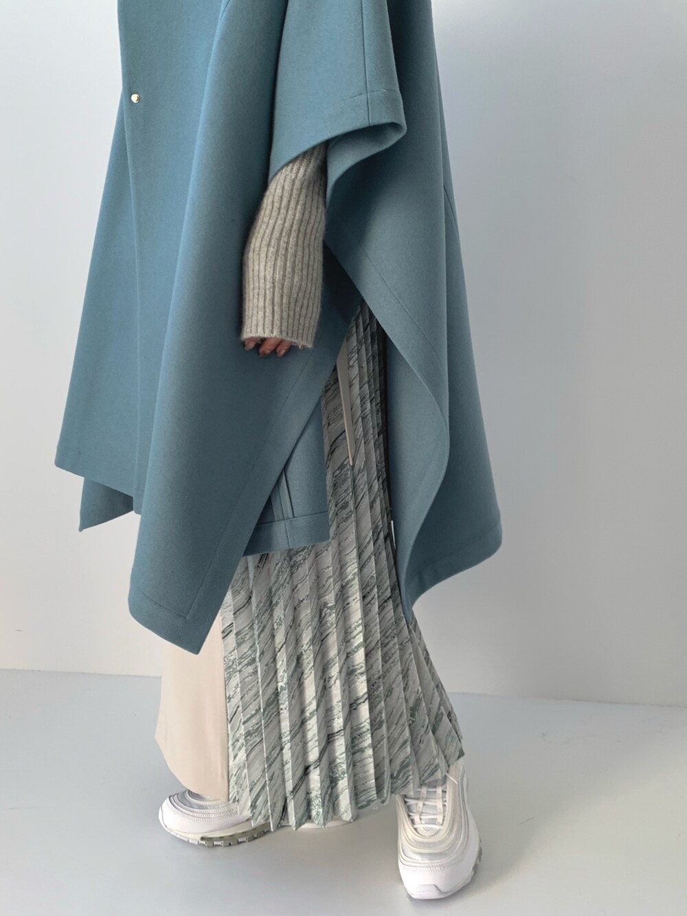 グレー系のステンカラーコート、グレー系のニット/セーター、ホワイト系のスカートを着用したレディースの冬コーディネートの2枚目の写真