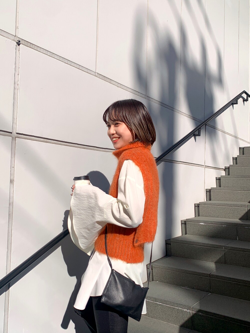 ブラック系のその他パンツ、オレンジ系のベスト、ホワイト系のシャツ/ブラウスを着用したレディースの冬コーディネートの3枚目の写真