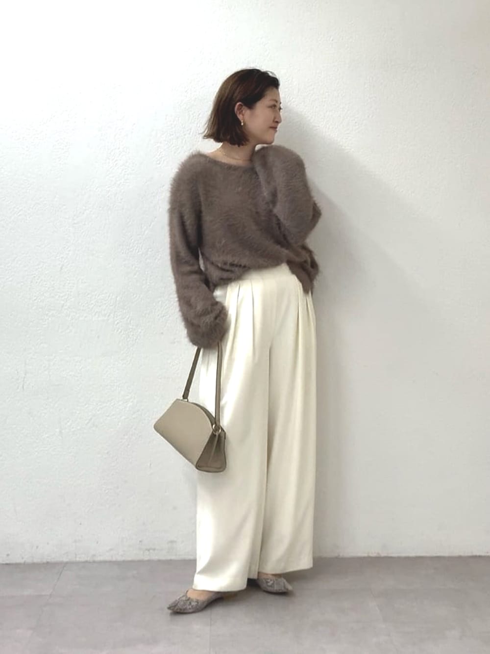 ブラウン系のニット/セーター、ホワイト系のスラックス、ベージュ系のハンドバッグを着用したレディースの秋コーディネートの3枚目の写真