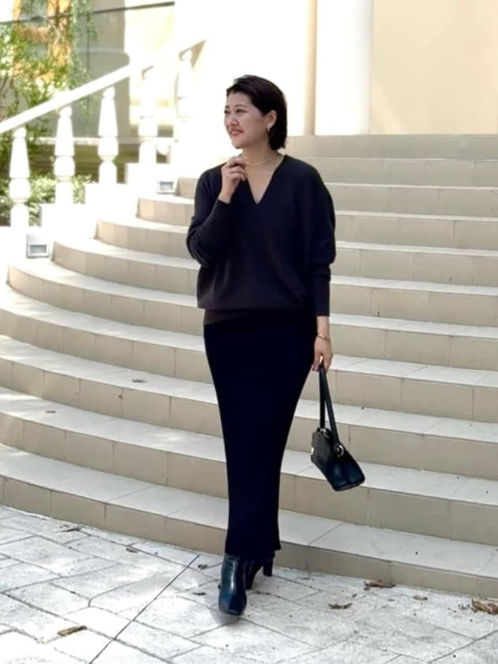 グレー系のニット/セーター、ブラック系のハンドバッグ、ブラック系のスカートを着用したレディースの秋コーディネートの2枚目の写真