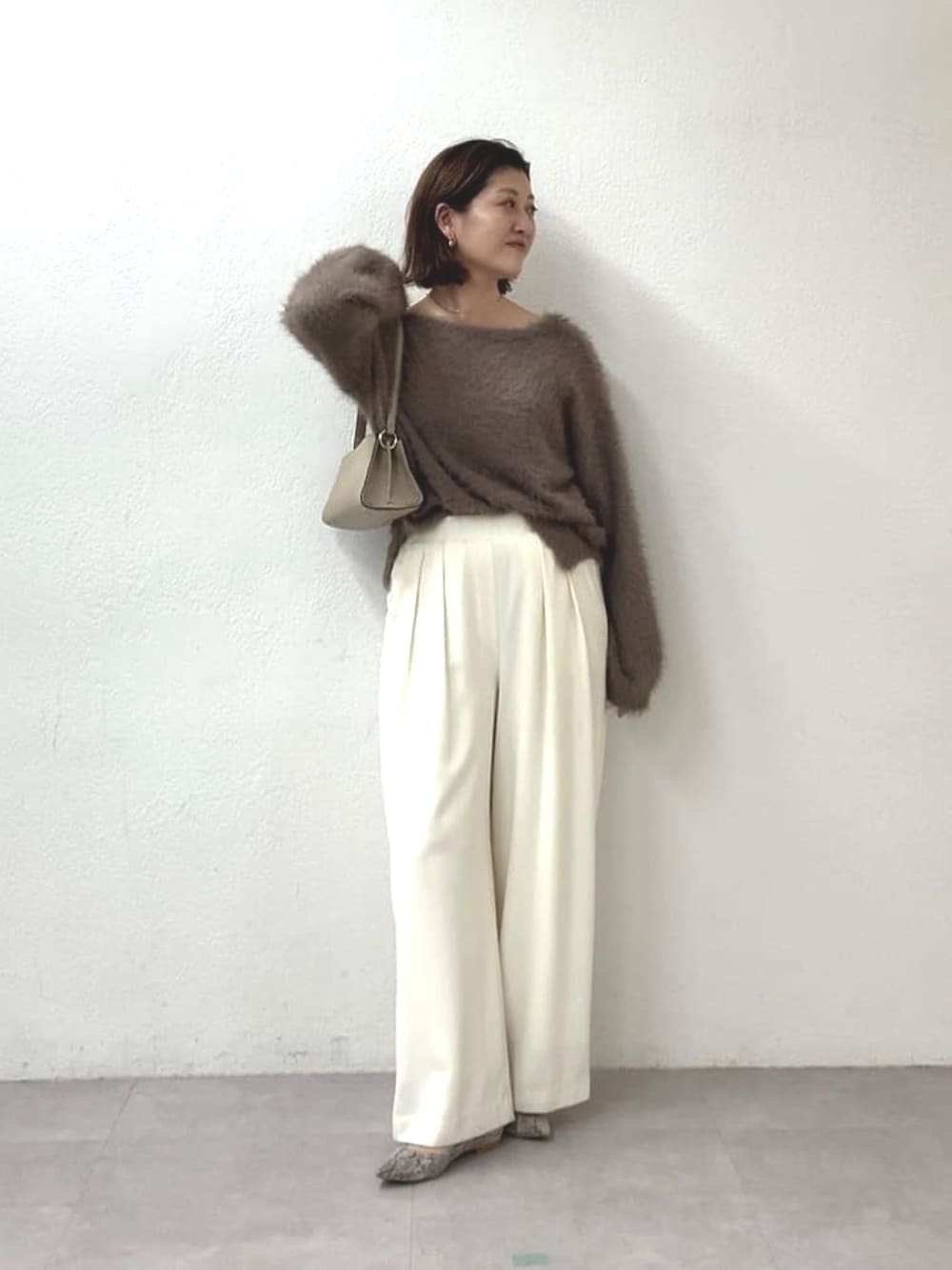 ブラウン系のニット/セーター、ホワイト系のスラックス、ベージュ系のハンドバッグを着用したレディースの秋コーディネートの2枚目の写真