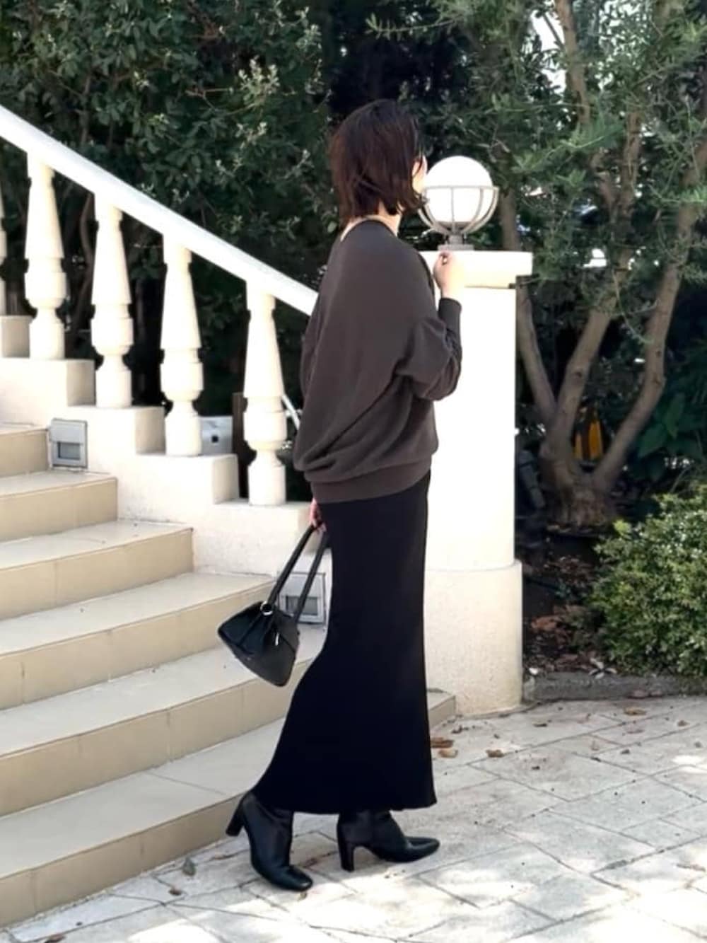 グレー系のニット/セーター、ブラック系のハンドバッグ、ブラック系のスカートを着用したレディースの秋コーディネートの3枚目の写真