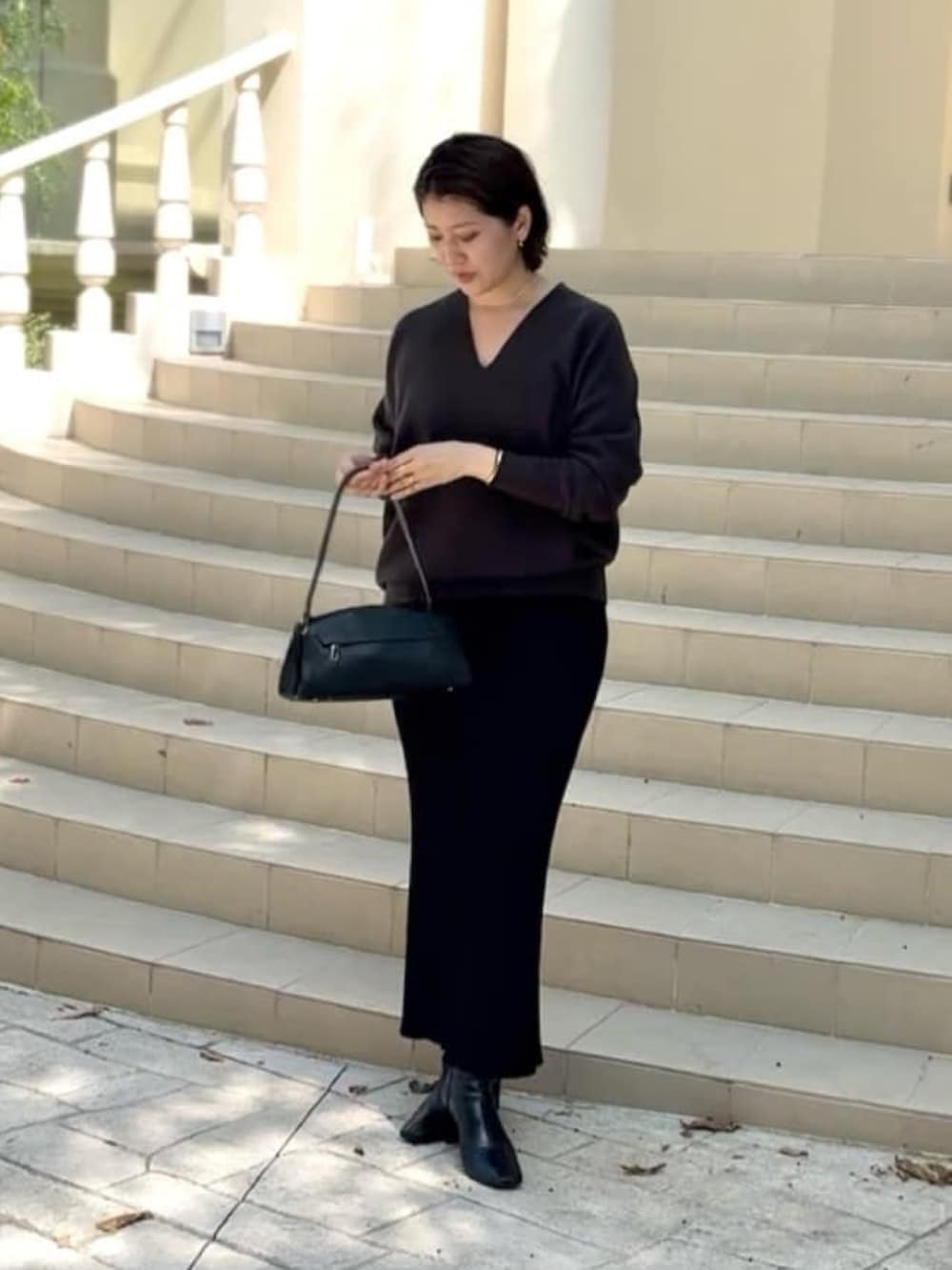 グレー系のニット/セーター、ブラック系のハンドバッグ、ブラック系のスカートを着用したレディースの秋コーディネートの4枚目の写真