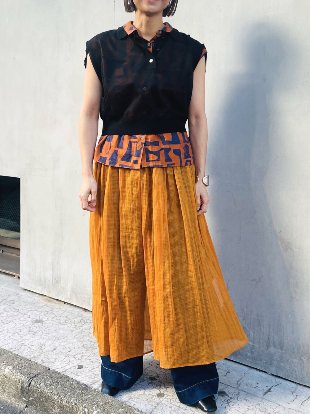 ブラック系のニット/セーター、オレンジ系のスカート、ブラウン系のシャツ/ブラウスを着用したレディースの春コーディネートの2枚目の写真