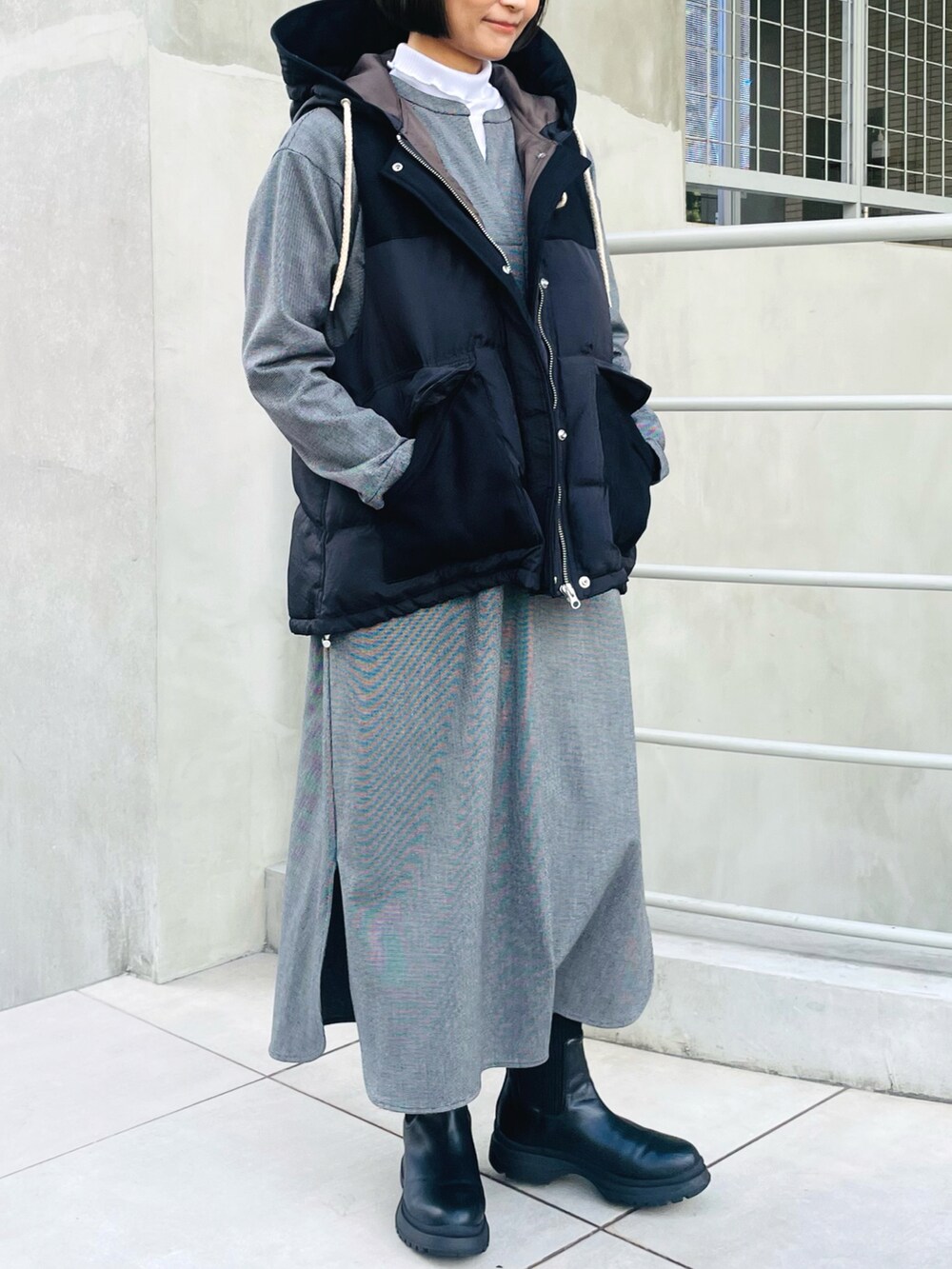 ブラック系のダウンベスト、ブラック系のワンピース、ホワイト系のTシャツ/カットソーを着用したレディースの冬コーディネートの2枚目の写真