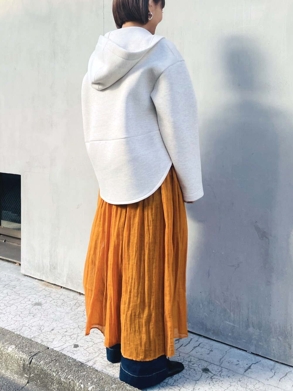 ベージュ系のパーカー、オレンジ系のスカート、ブラウン系のシャツ/ブラウスを着用したレディースの春コーディネートの2枚目の写真