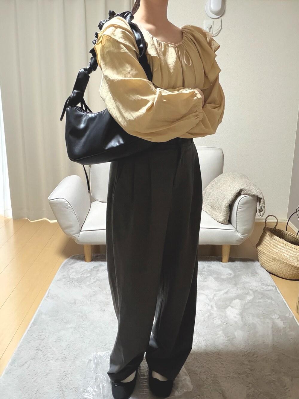イエロー系のトップス、グレー系のパンツ、ブラック系のバッグを着用したレディースの春コーディネートの2枚目の写真