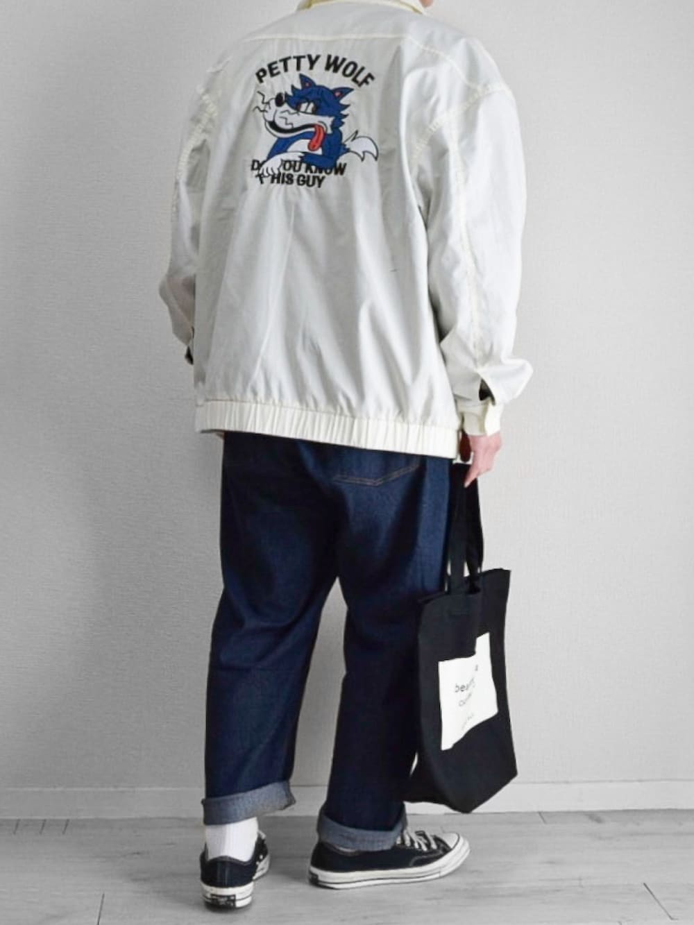 ホワイト系のブルゾン、ブルー系のデニムパンツ、ブラック系のトートバッグを着用したメンズの春コーディネートの2枚目の写真