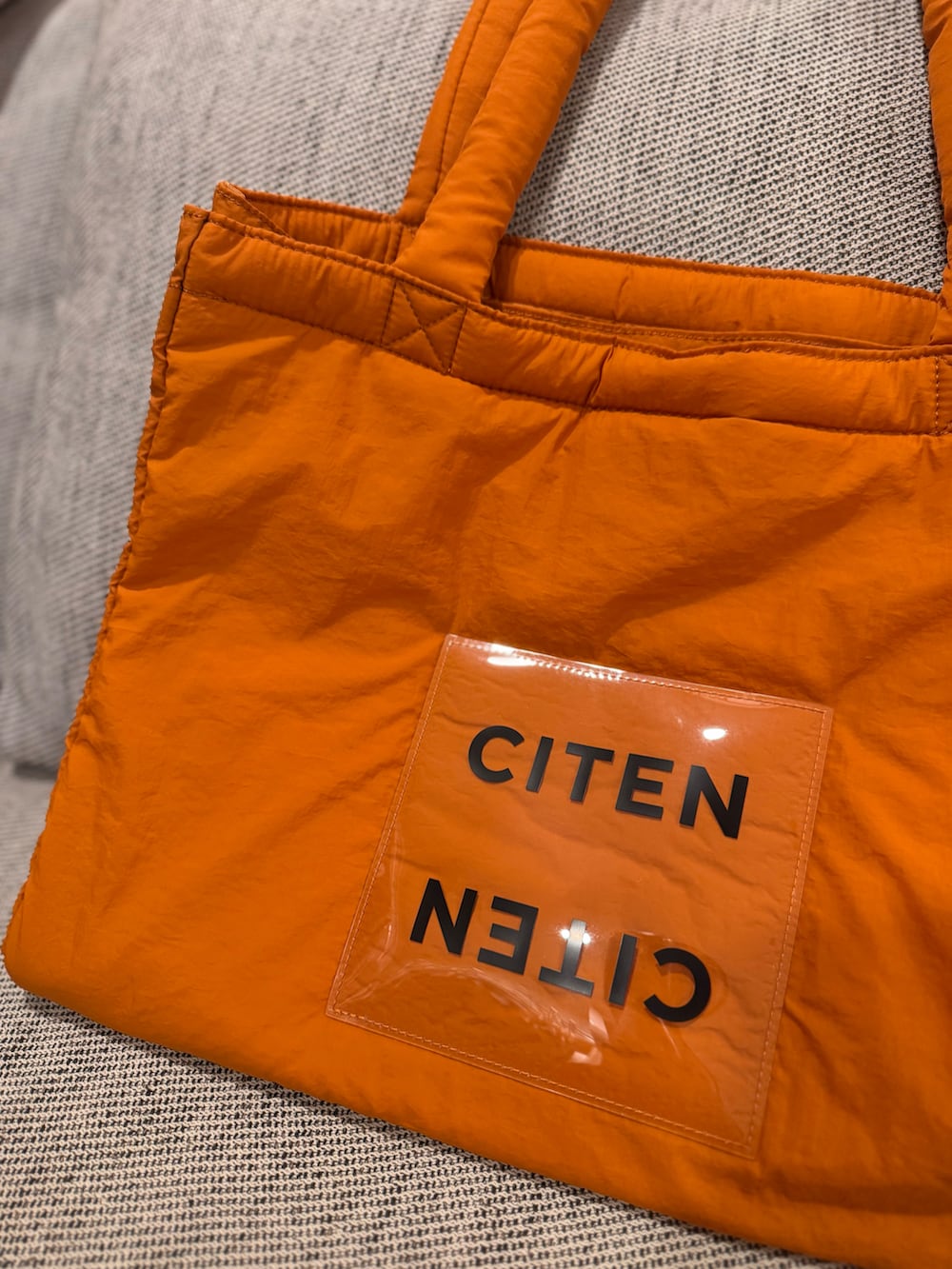 オレンジ系のトートバッグ、ブラック系のスリッポン、グレー系のトップスを着用したレディースの秋コーディネートの3枚目の写真