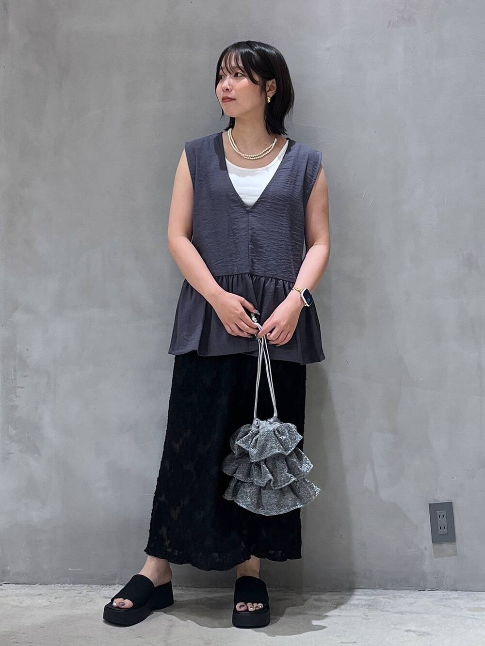 シルバー系のショルダーバッグ、ブラック系のサンダル、ブラック系のスカートを着用したレディースの夏コーディネートの2枚目の写真