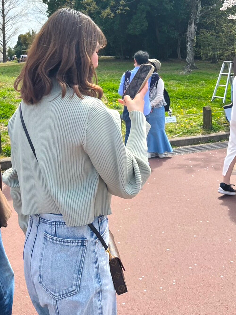 ブラック系のデニムパンツ、グリーン系のカーディガン/ボレロ、ホワイト系のスニーカーを着用したレディースの春コーディネートの2枚目の写真