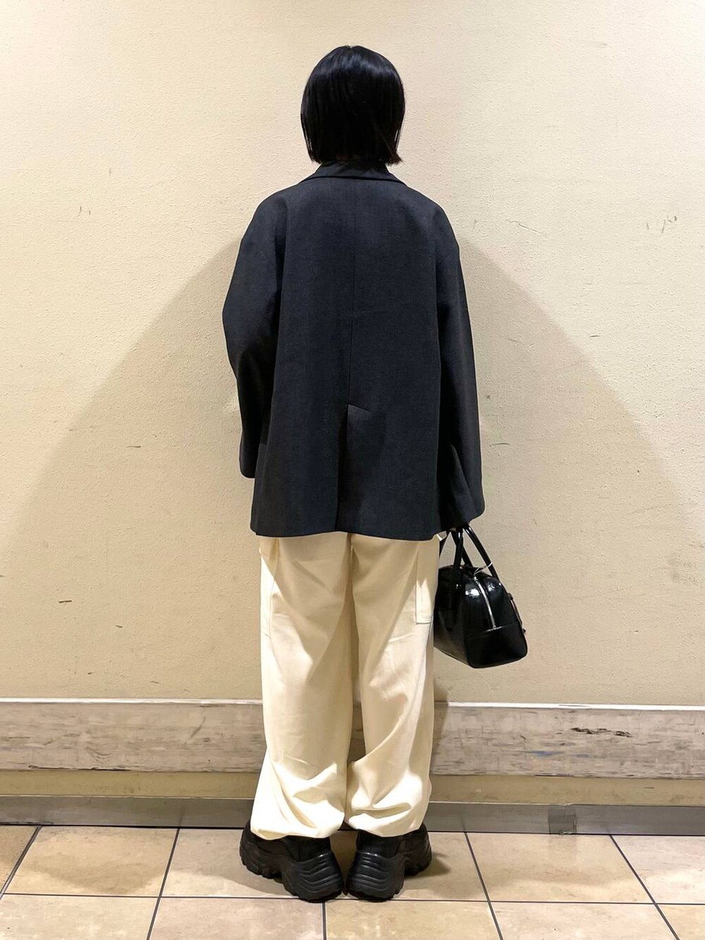 グレー系のテーラードジャケット、ブラック系のボストンバッグ、ホワイト系のその他パンツを着用したレディースの秋コーディネートの2枚目の写真
