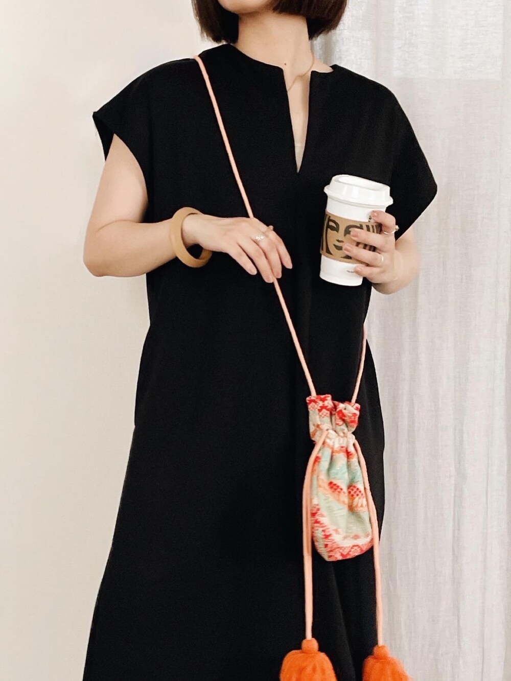 ブラック系のワンピース、ブラック系のサンダル、オレンジ系のショルダーバッグを着用したレディースの夏コーディネートの3枚目の写真