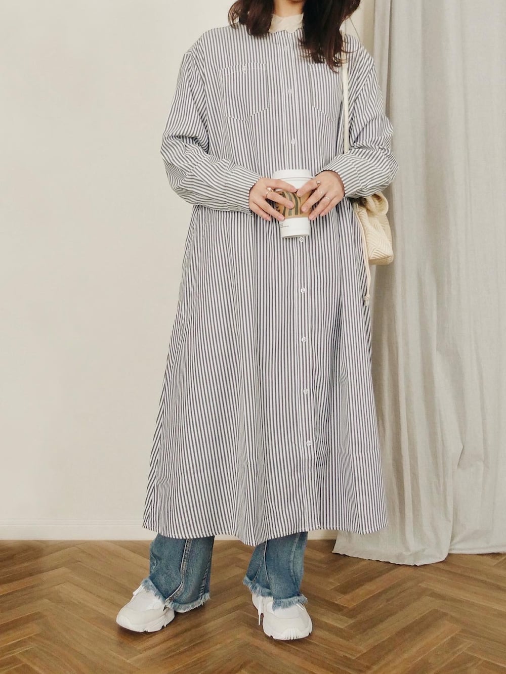 ブラック系のシャツワンピース、ホワイト系のショルダーバッグ、ブルー系のデニムパンツを着用したレディースの冬コーディネートの2枚目の写真